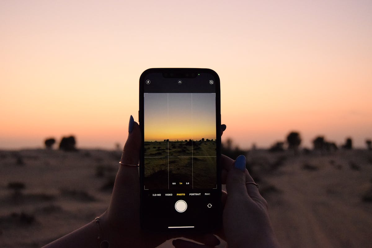 Person holding an iPhone with the camera app open, capturing a sunset landscape with grid lines enabled